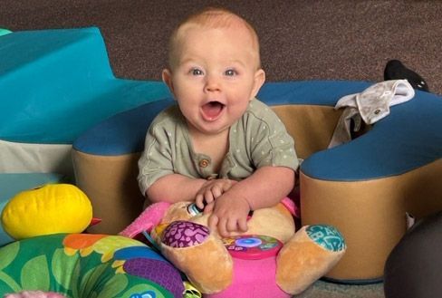 Happy infant playing with soft toys in a structured Montessori environment.