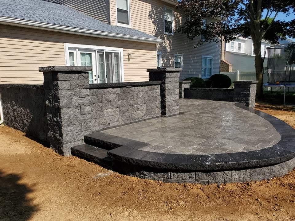 A patio with steps and a stone wall in front of a house.