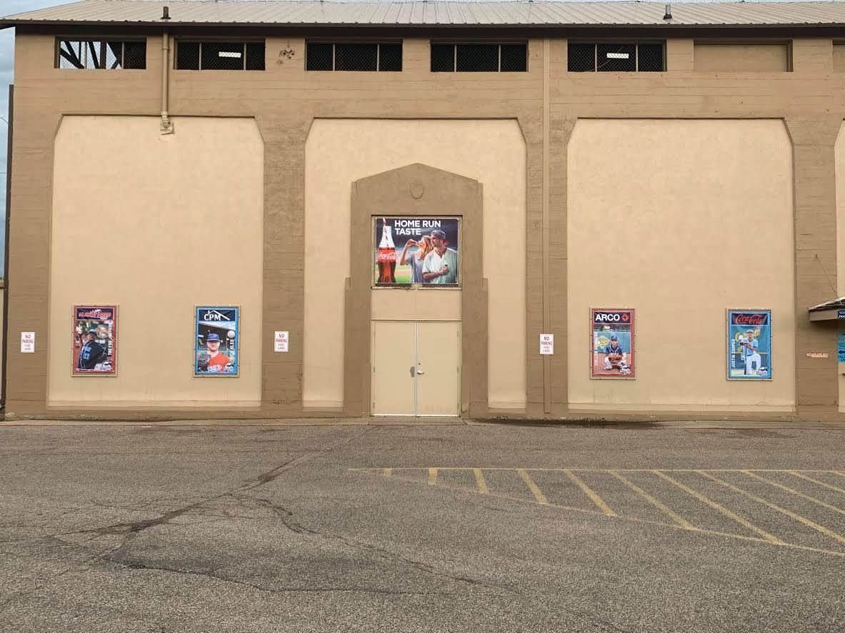 Tan brick building facade with posters and a central doorway over a parking lot.