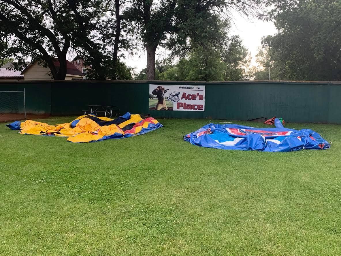 Several colorful deflated inflatable play structures on a grassy field behind a green fence.