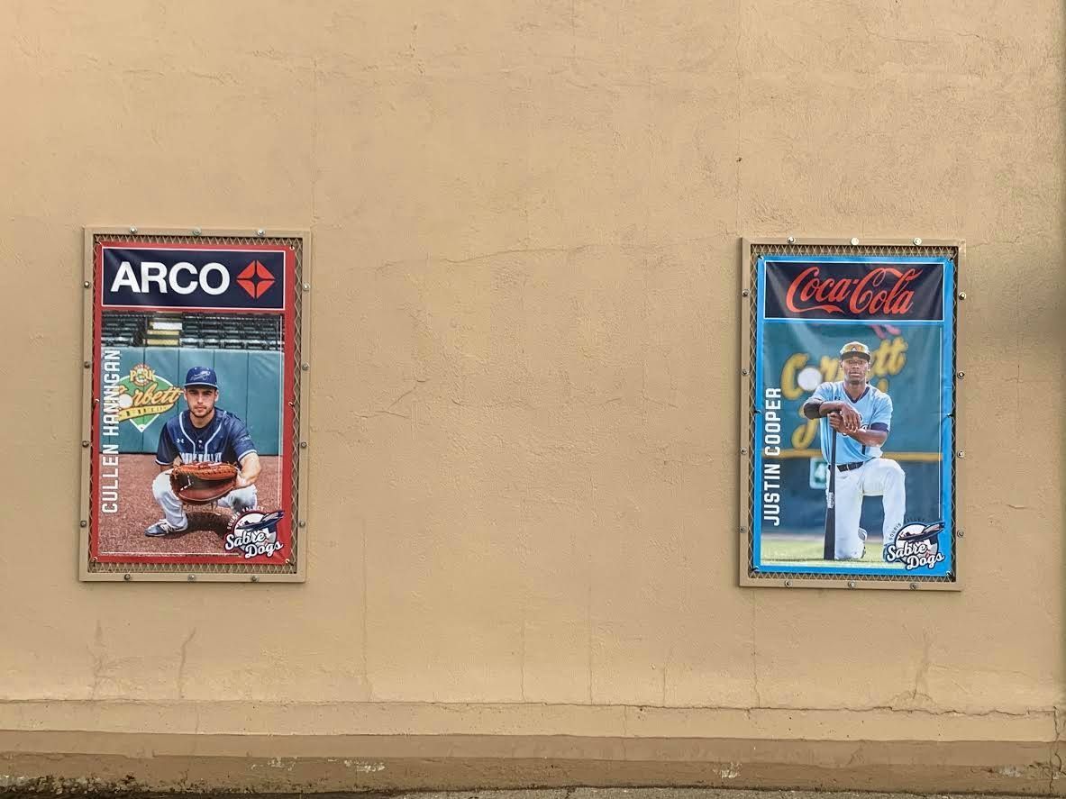 Two framed baseball cards mounted on a beige wall, one ARCO and one Coca-Cola themed.