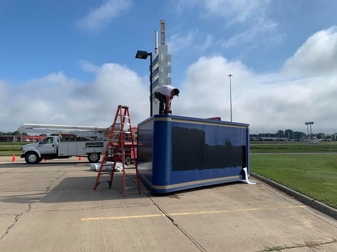 Red ladder beside a blue shipping container with a worker on top near a runway.