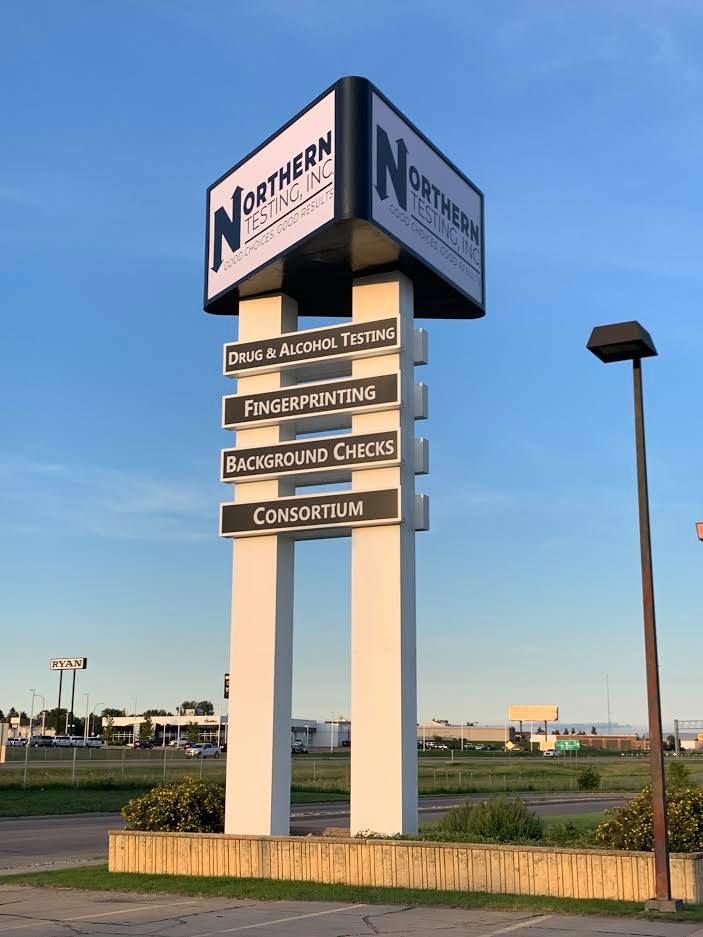 Tall illuminated business sign with directional panels at roadside under a blue sky.