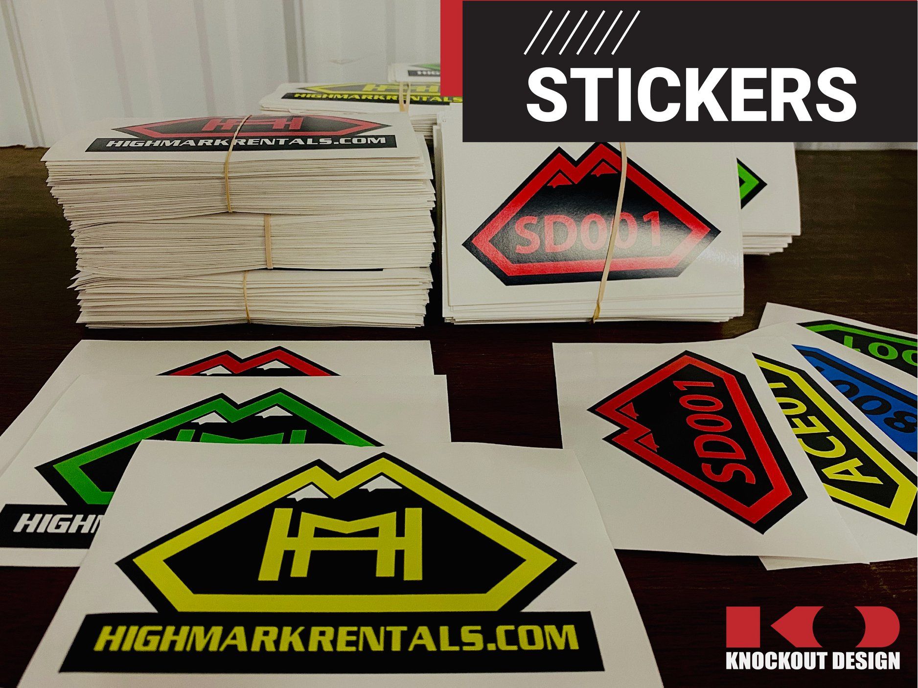 Assorted custom logo stickers on a table, including stacks and colorful decals with bold branding.