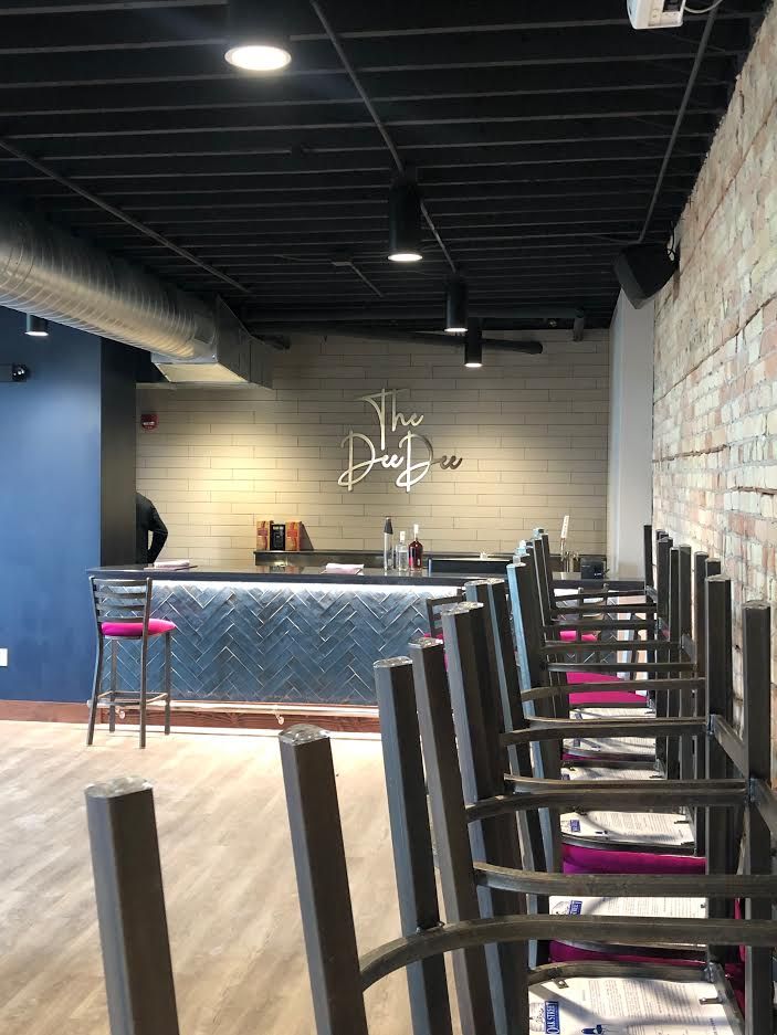 Empty bar interior with black chairs, a blue counter, and a brick wall