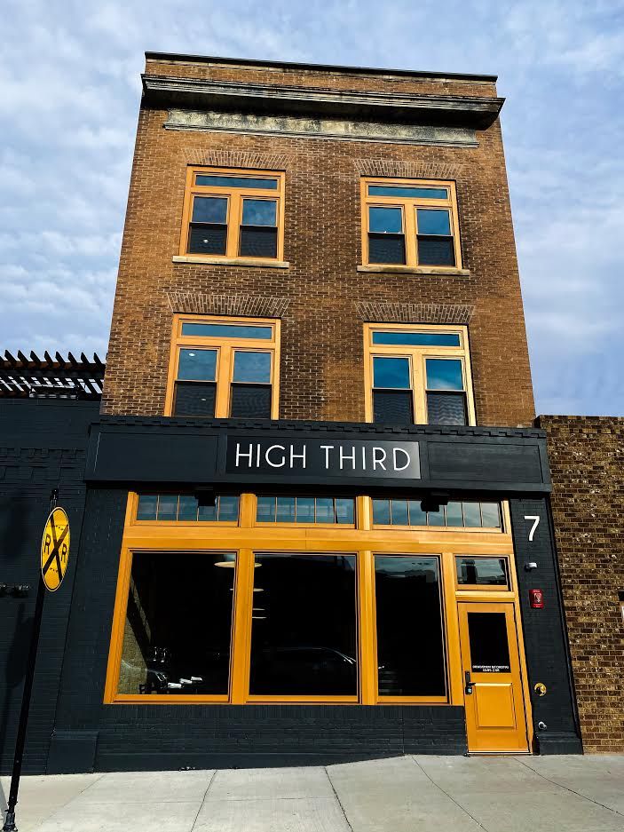 Brick building with black storefront sign reading “HIGH THIRD” and orange-trimmed windows and door