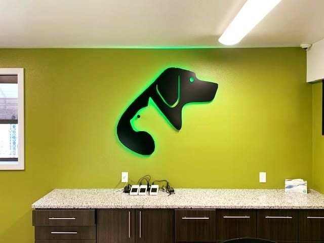 Office kitchenette with lime green wall and black dog silhouette logo above a countertop and cabinets