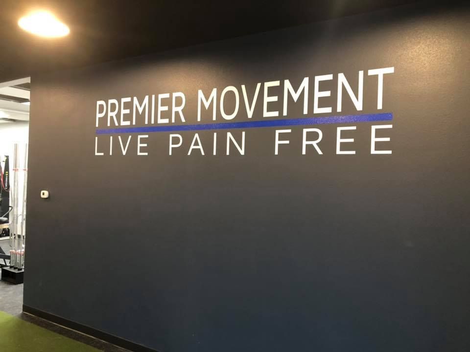 Wall with “Premier Movement” and “Live Pain Free” signage in a dimly lit gym lobby