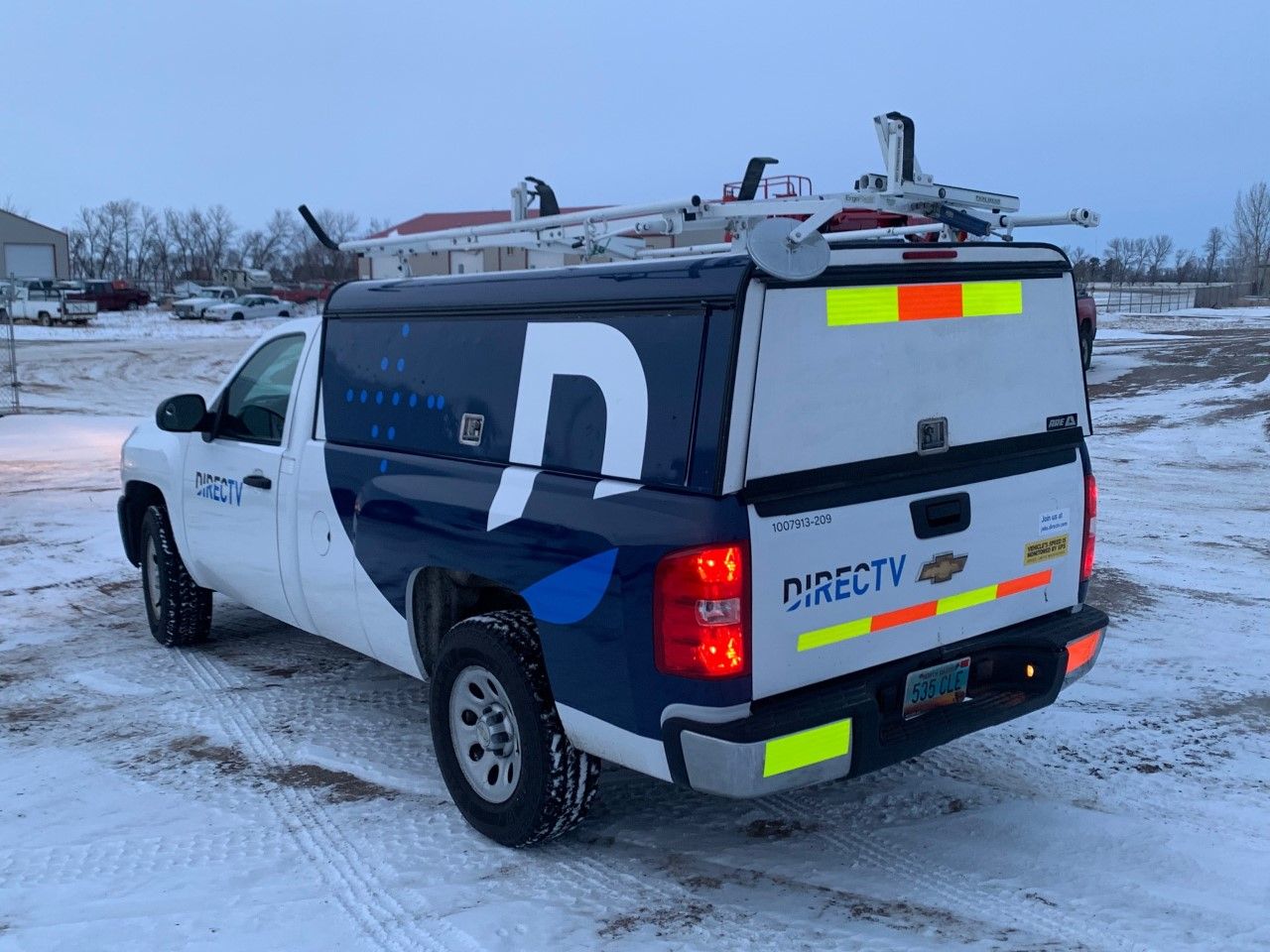 White utility pickup truck with rooftop equipment parked in a snowy lot, rear view with high-visibility markings