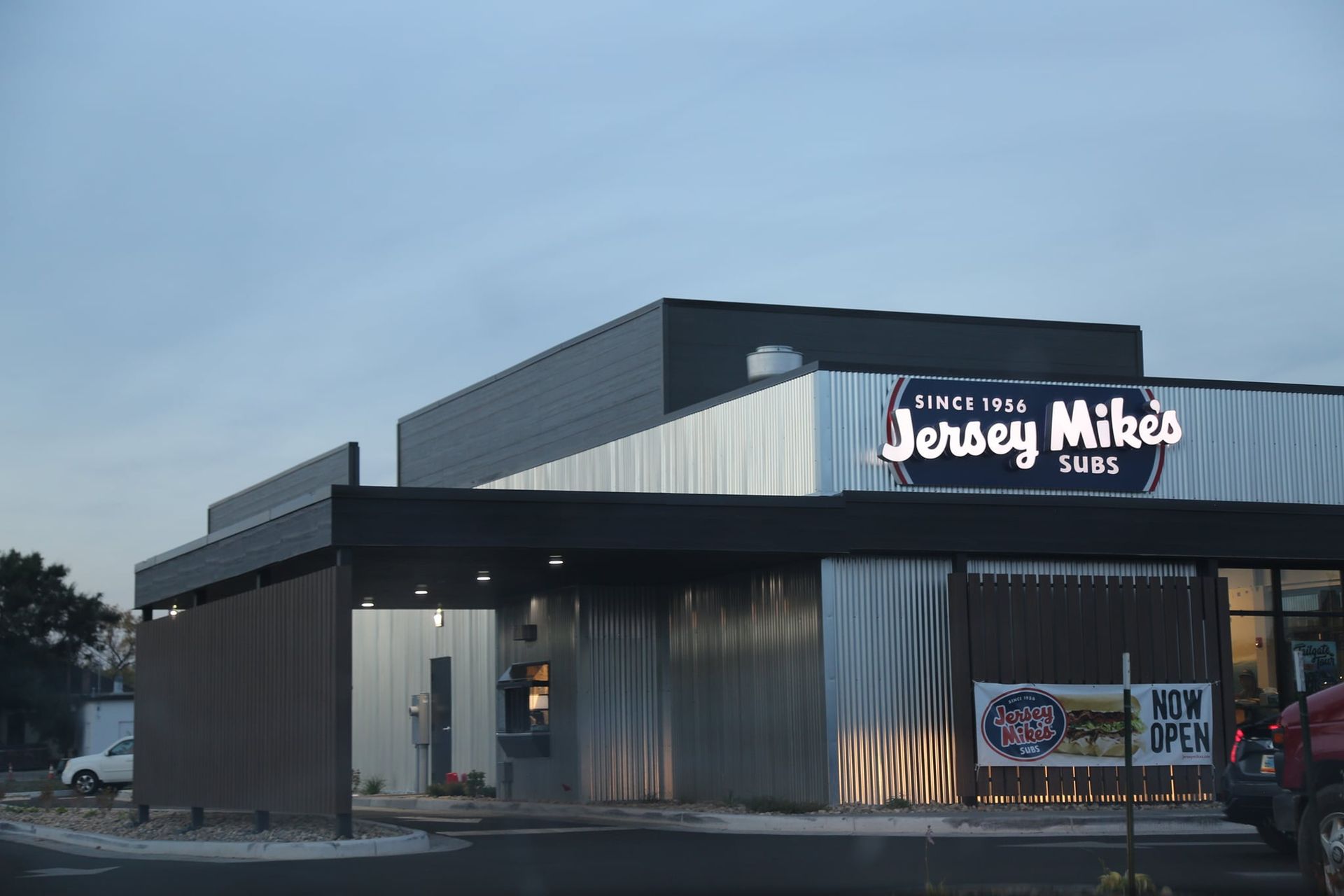 Exterior of Jersey Mike’s Subs at dusk, with lit sign and storefront windows