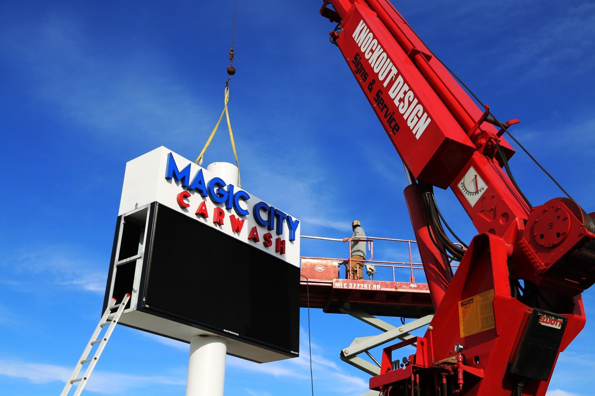 Crane lifting a MAGIC CITY sign onto a pole under a clear blue sky