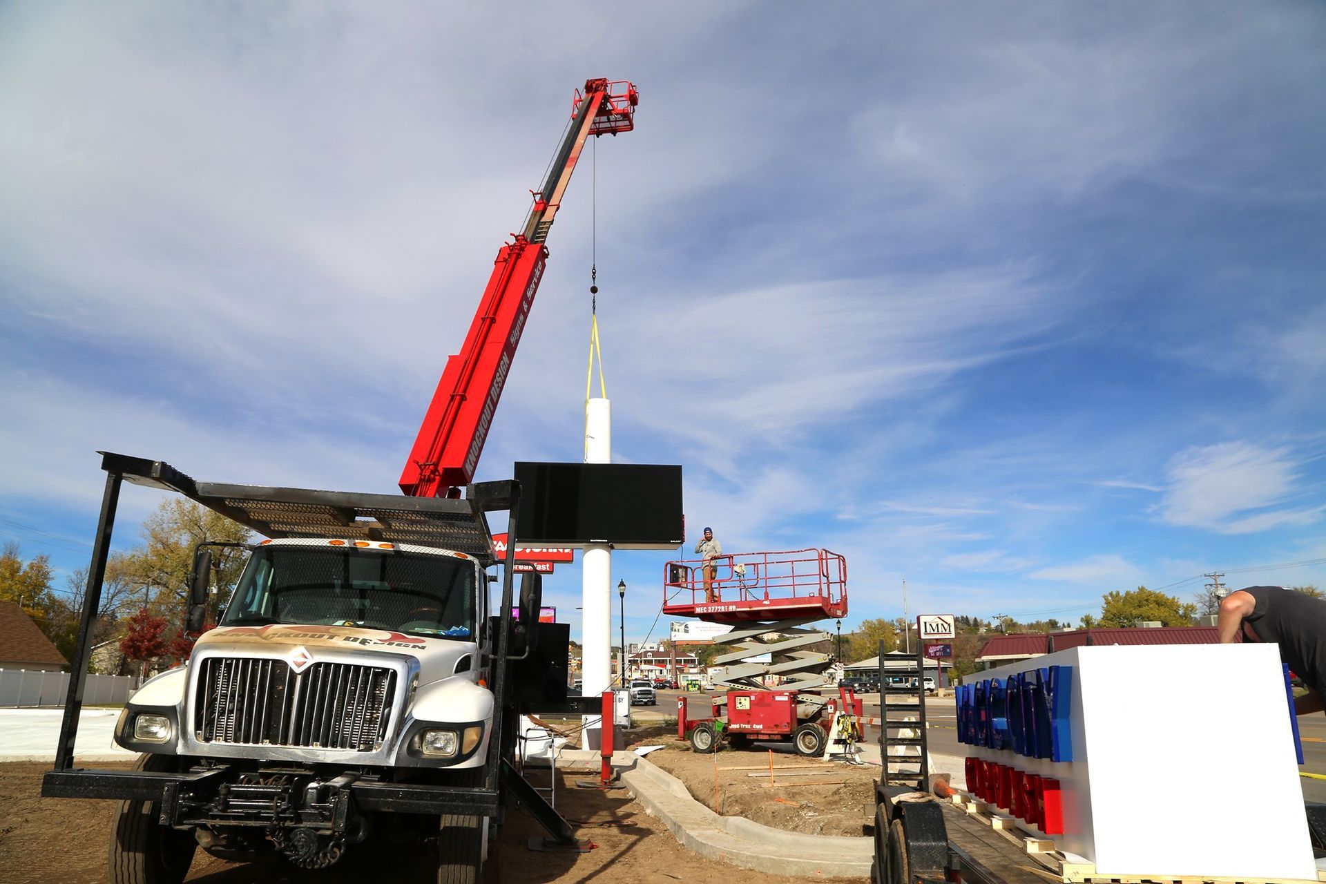 Construction site with trucks and a red crane lifting equipment under a cloudy sky