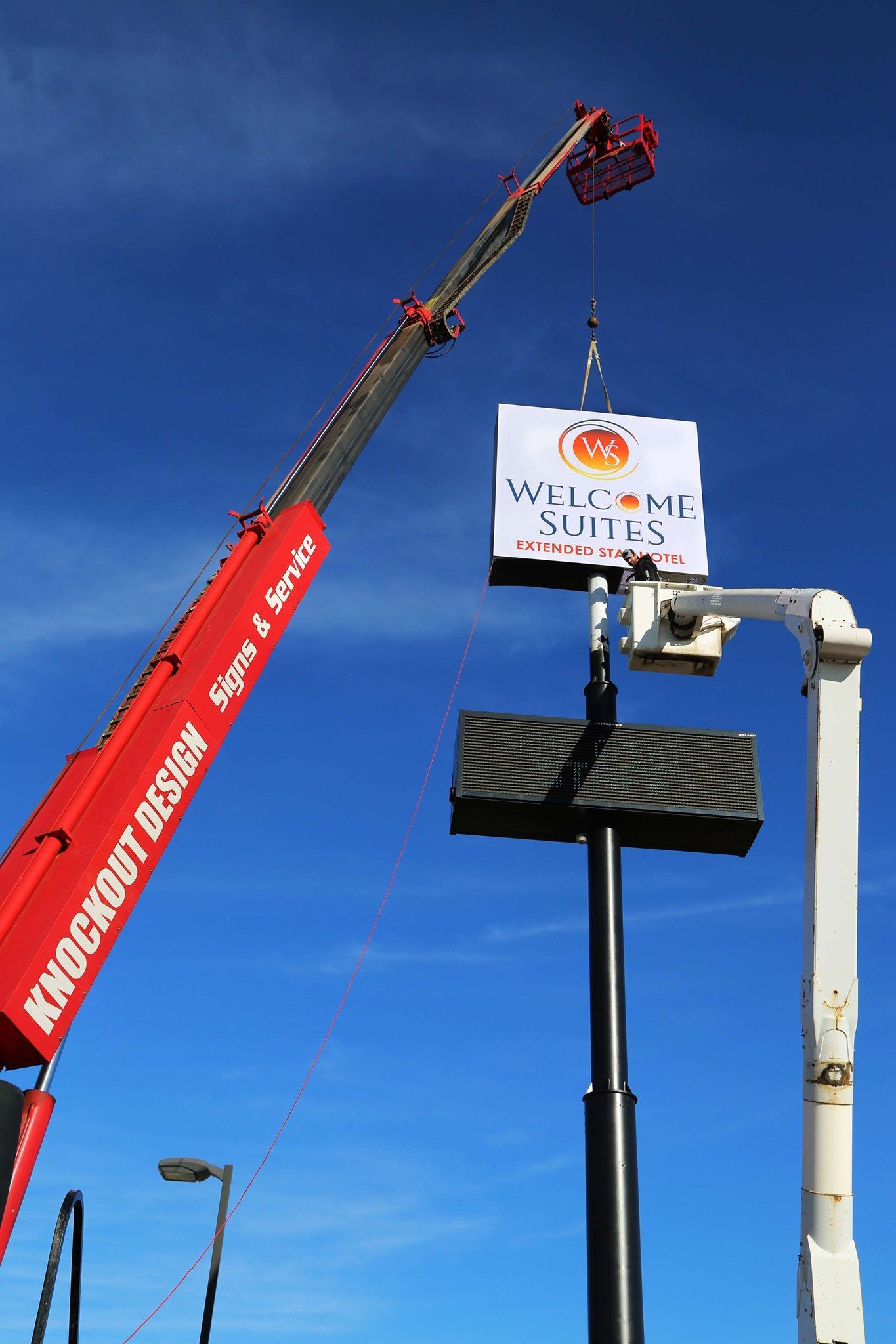 Red crane and black lift arm beside a sign against a clear blue sky