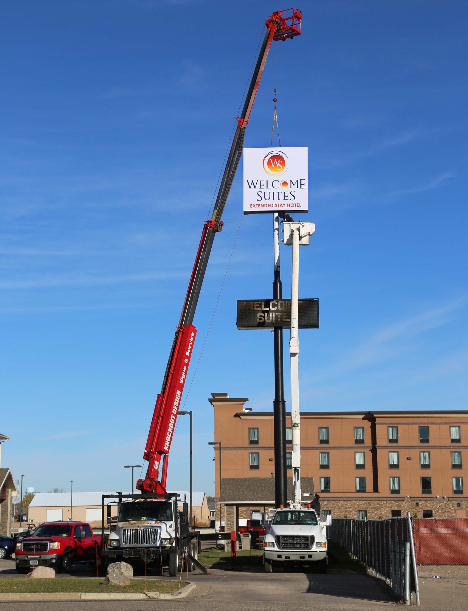 Red crane lifting a sign beside a brick building under a clear blue sky