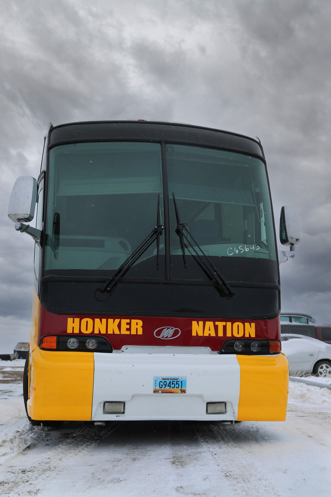 Front view of a black and yellow bus parked on snow under a cloudy sky
