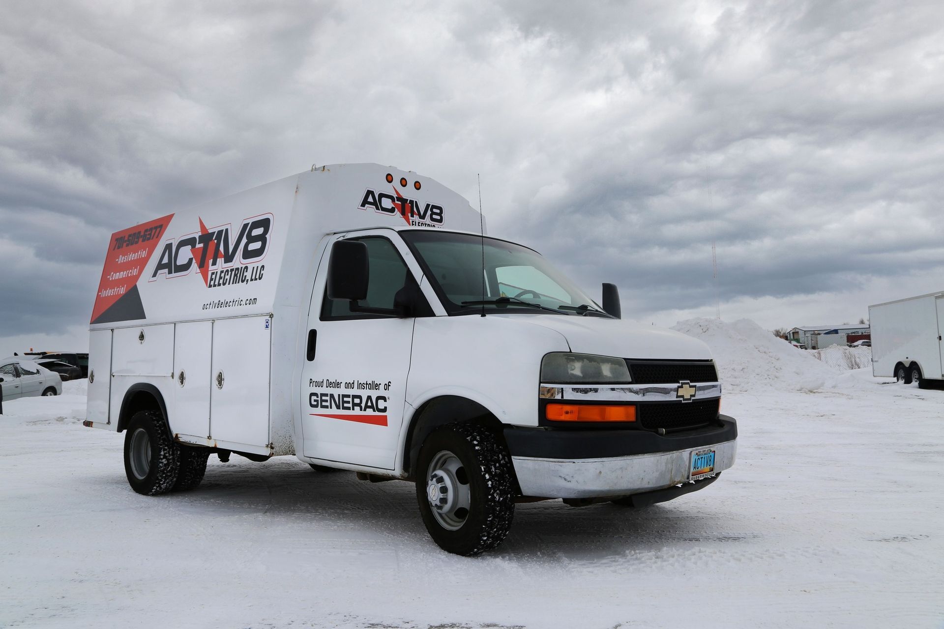 White utility van driving on snowy road under overcast sky, with company logos on the sides