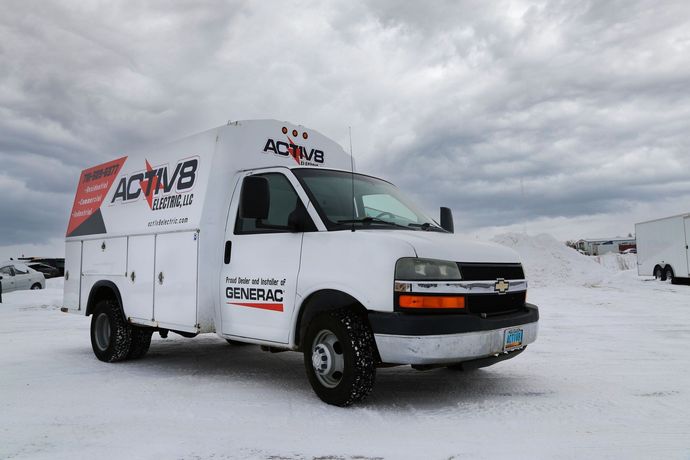 White utility van driving on snowy road under overcast sky, with company logos on the sides