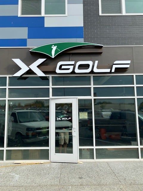 X Golf storefront with large logo above glass entrance and blue-gray facade