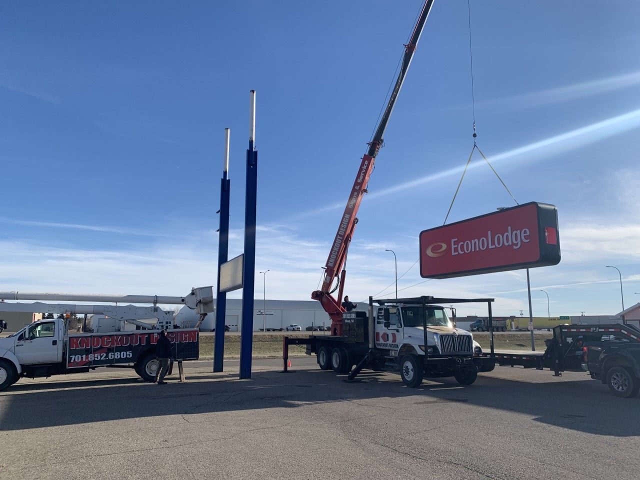 Crane lifting a Cargill sign beside trucks and tall blue poles on a waterfront lot