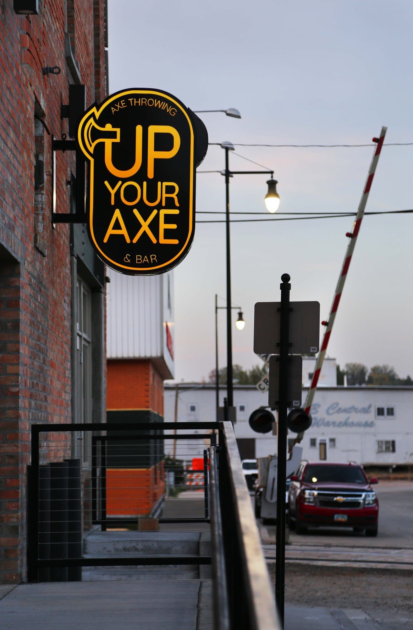 Neon “Up Your Axe” sign on a brick building along a city street at dusk