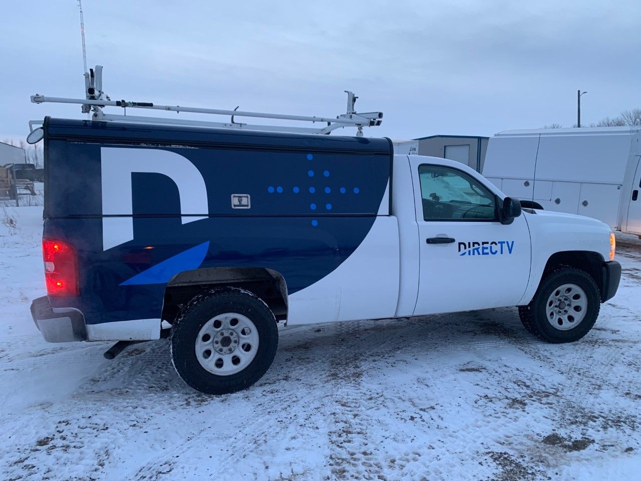 DirecTV service van parked in a snowy lot, white and dark blue with a large logo on the side