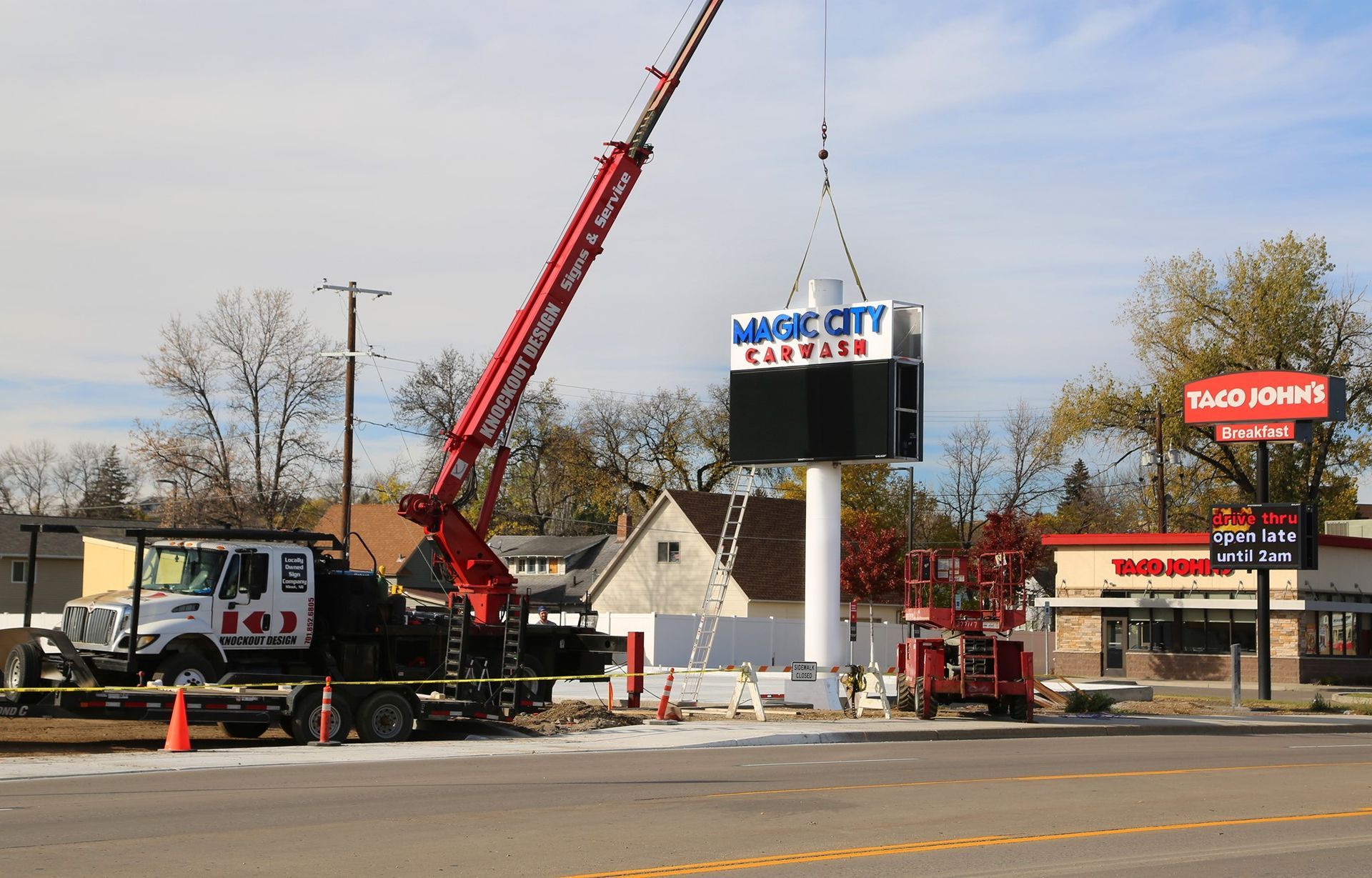 Crane lifting a large roadside sign beside a Burger King and other fast-food restaurants.