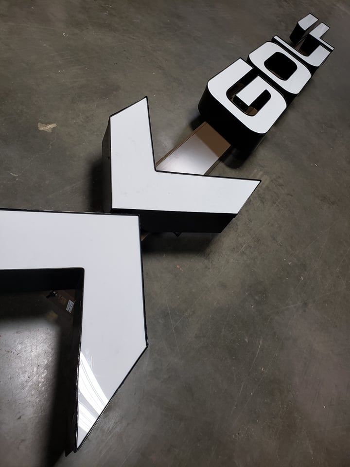 White and black arrow-shaped sign with bold letters on a concrete floor, pointing diagonally.