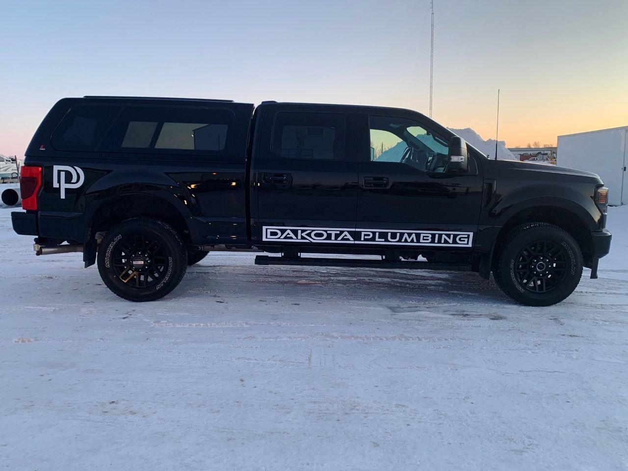 Black pickup truck with canopy and off-road tires parked on snow at sunset