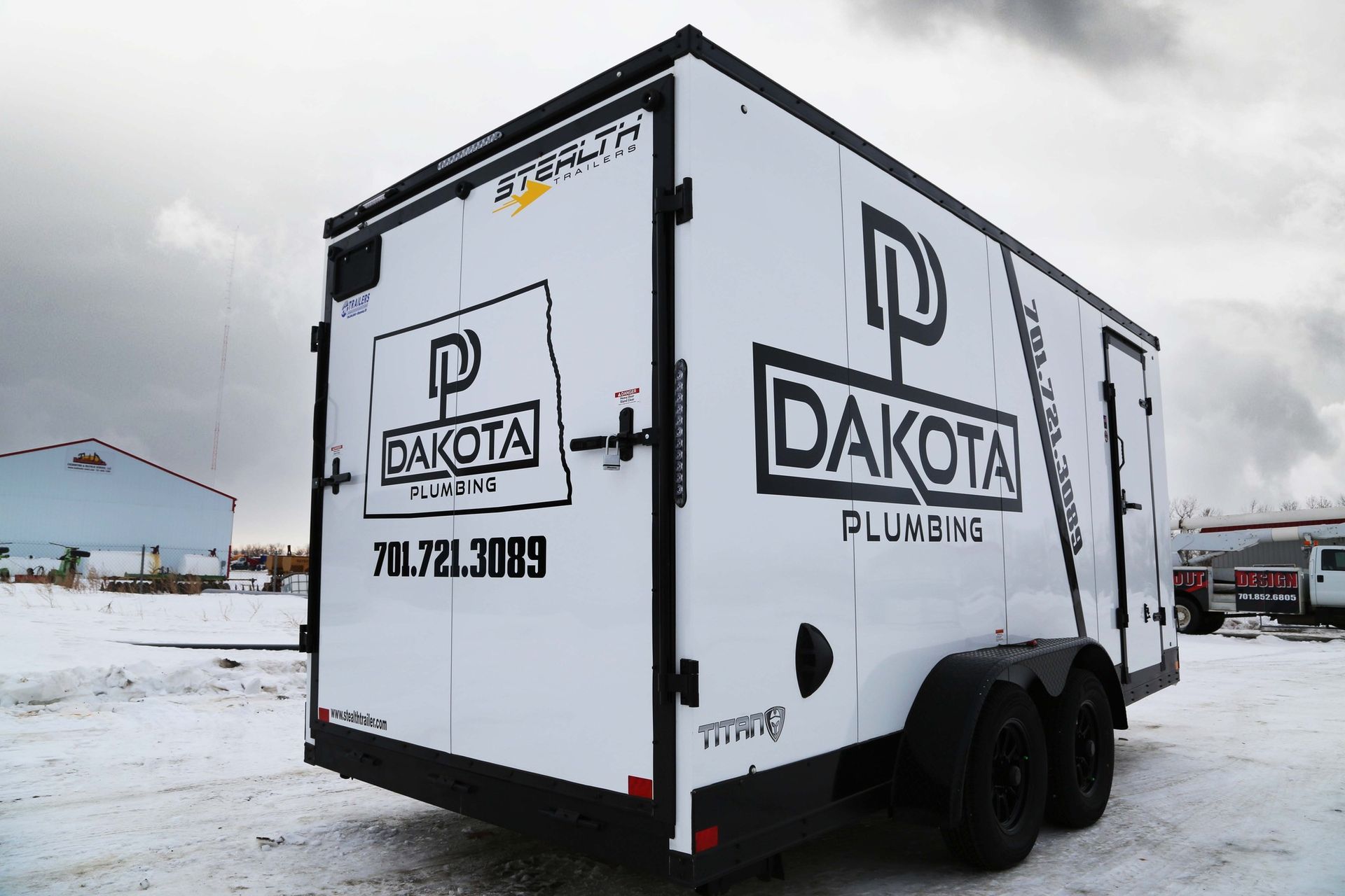 White Dakota Plumbing trailer parked in a snowy lot under an overcast sky.