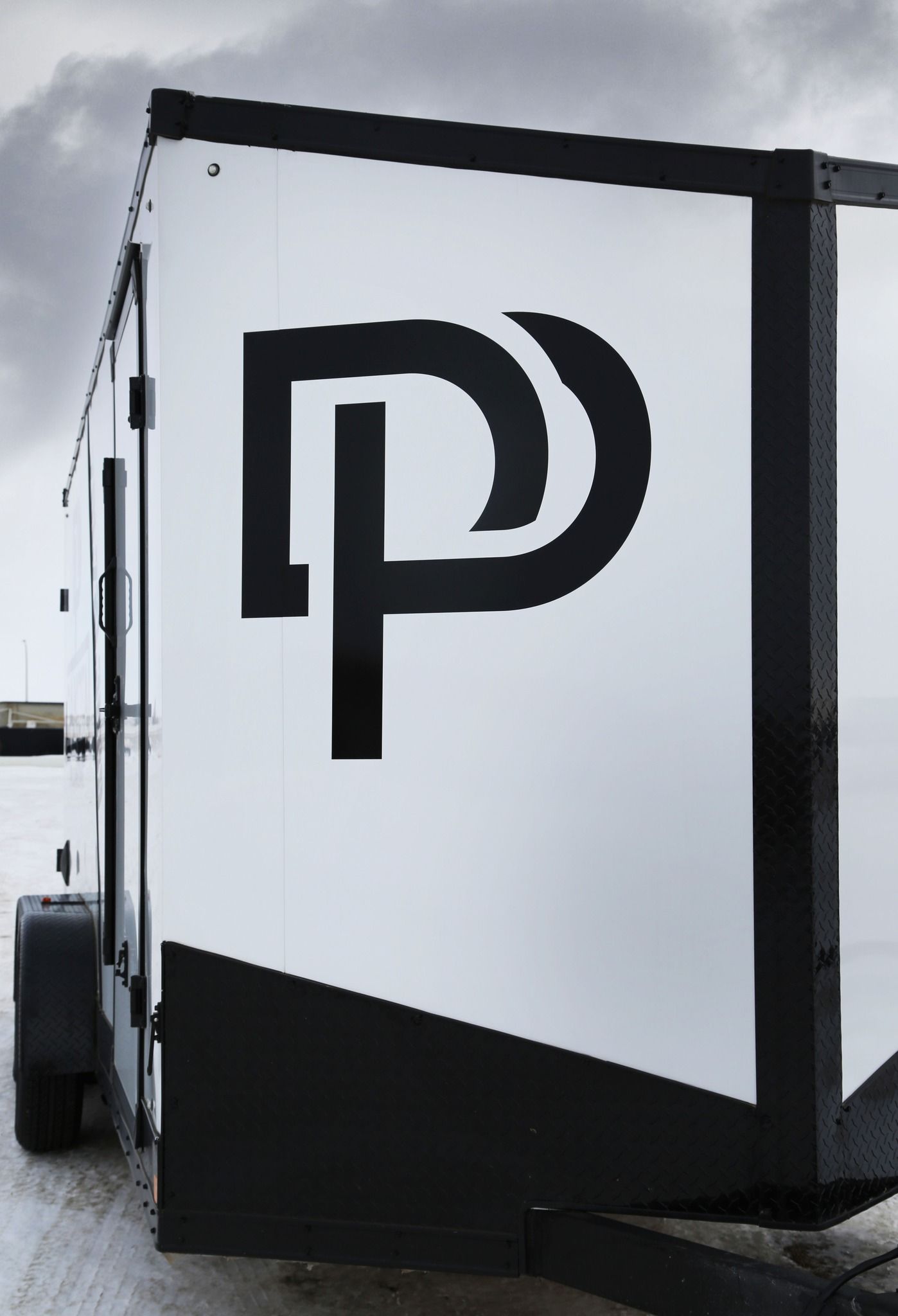 Black-and-white trailer side panel with a stylized “P” logo outdoors under a cloudy sky