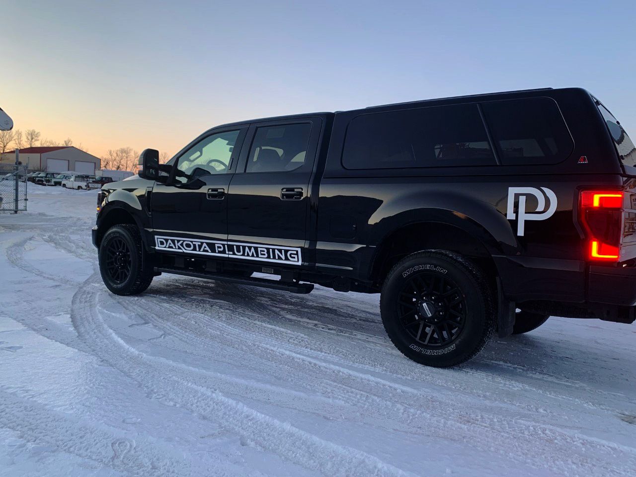 Black pickup truck parked on a snowy road at sunset, with bold white decals on the side.