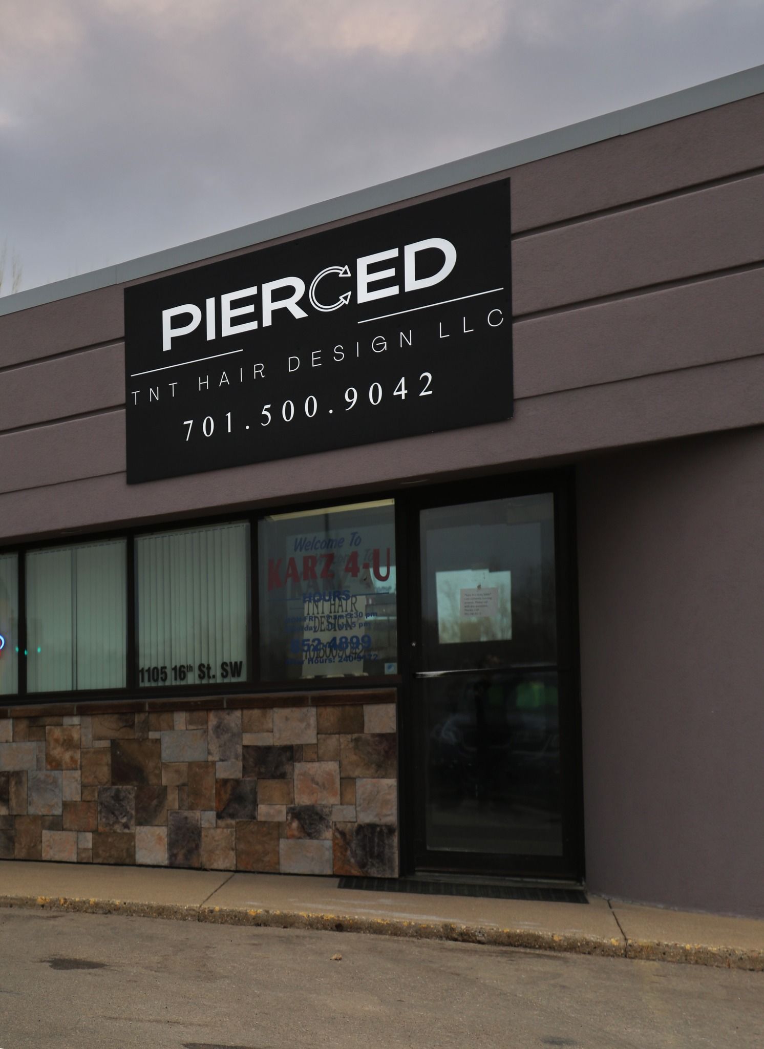Storefront with a black “PIERCED” sign above a window and glass door on a gray building.