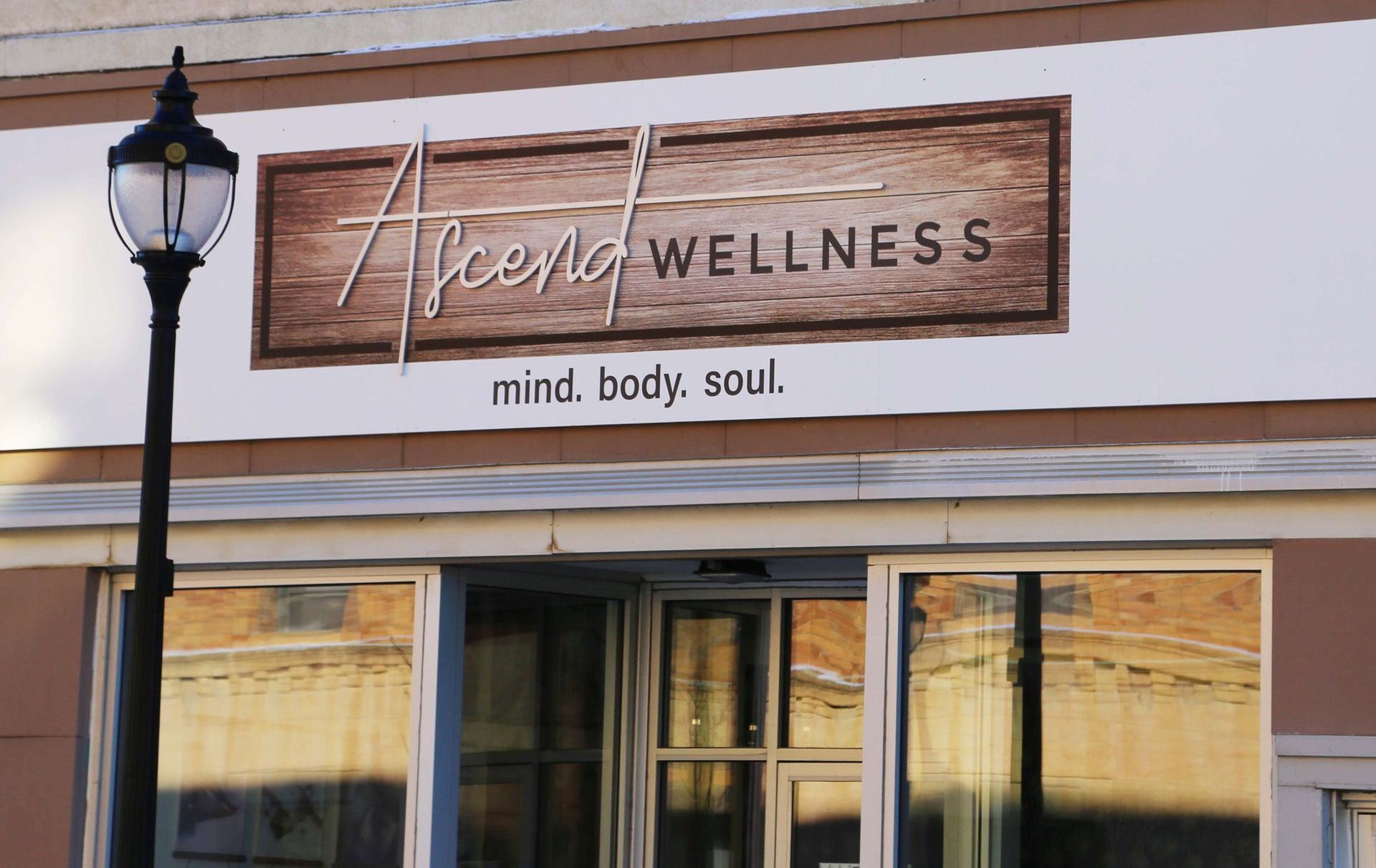 Aspen Wellness storefront sign on a beige building, with a streetlamp and glass entrance below.