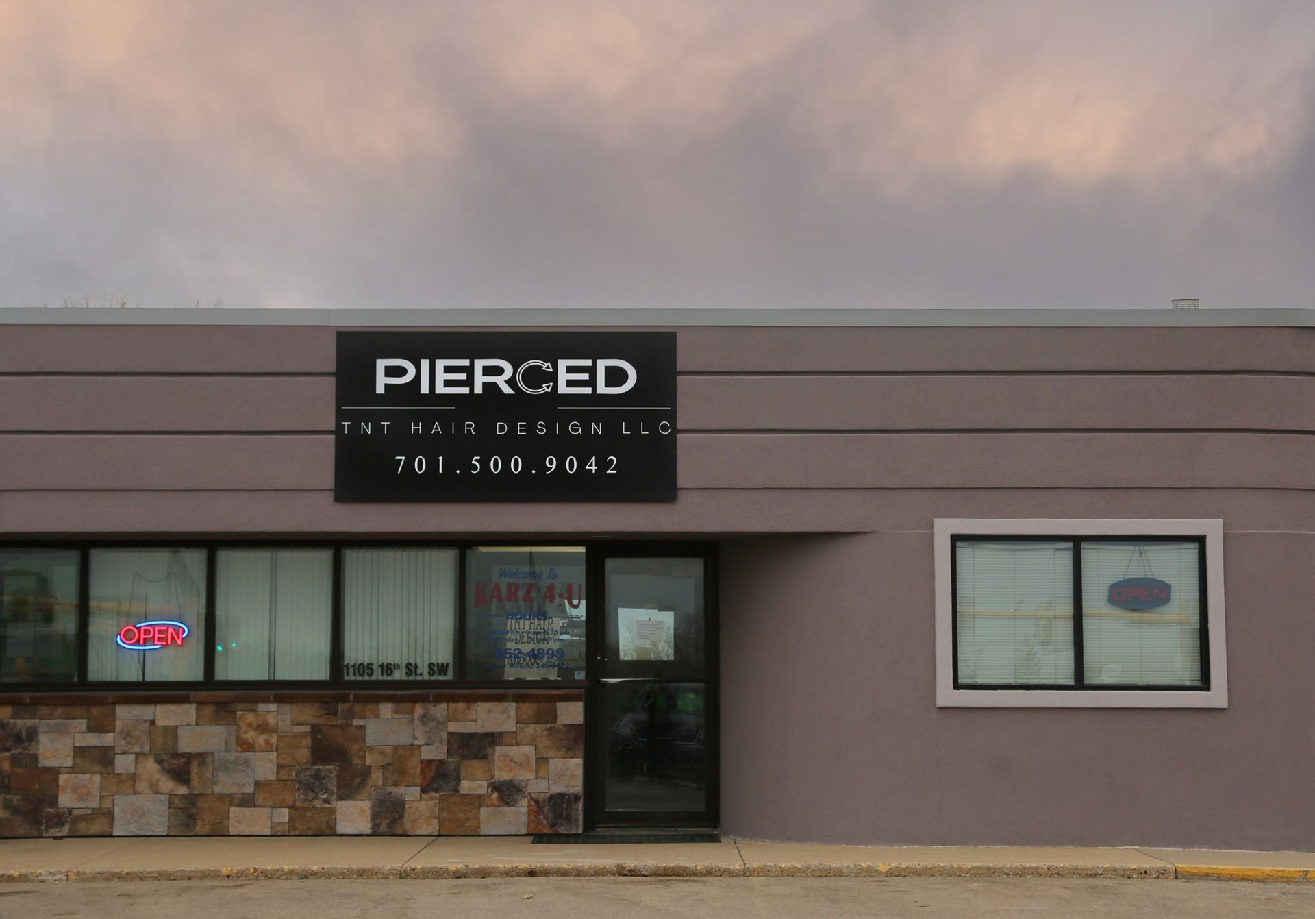 Pierced store front with stone facade, black sign, windows, and glass door under a cloudy sky.