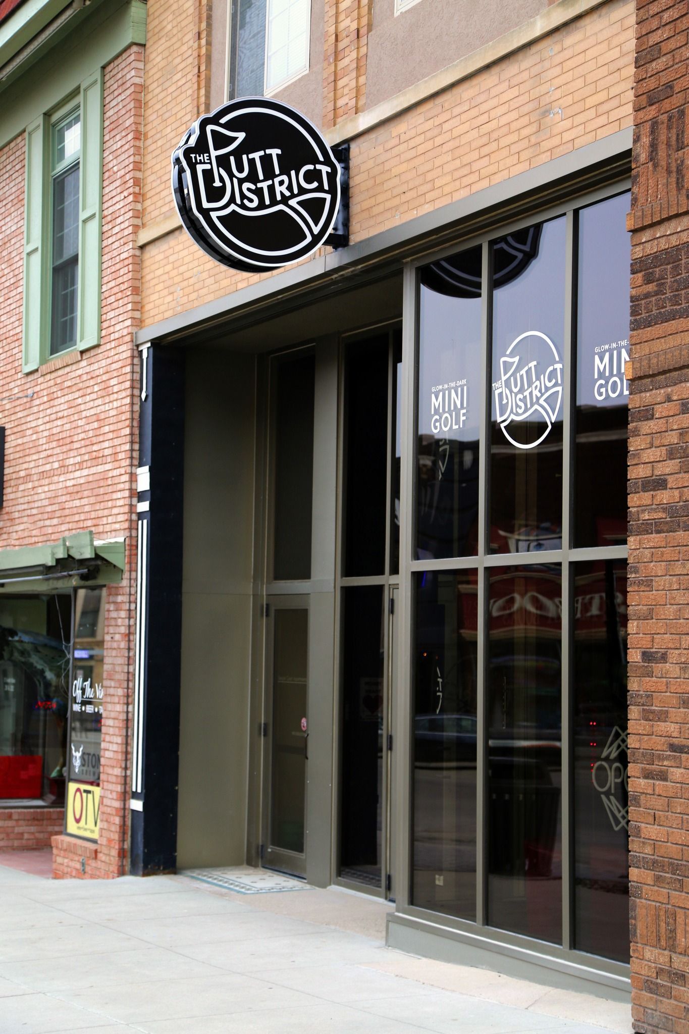 Brick storefront with a round black sign and large glass windows on the sidewalk.