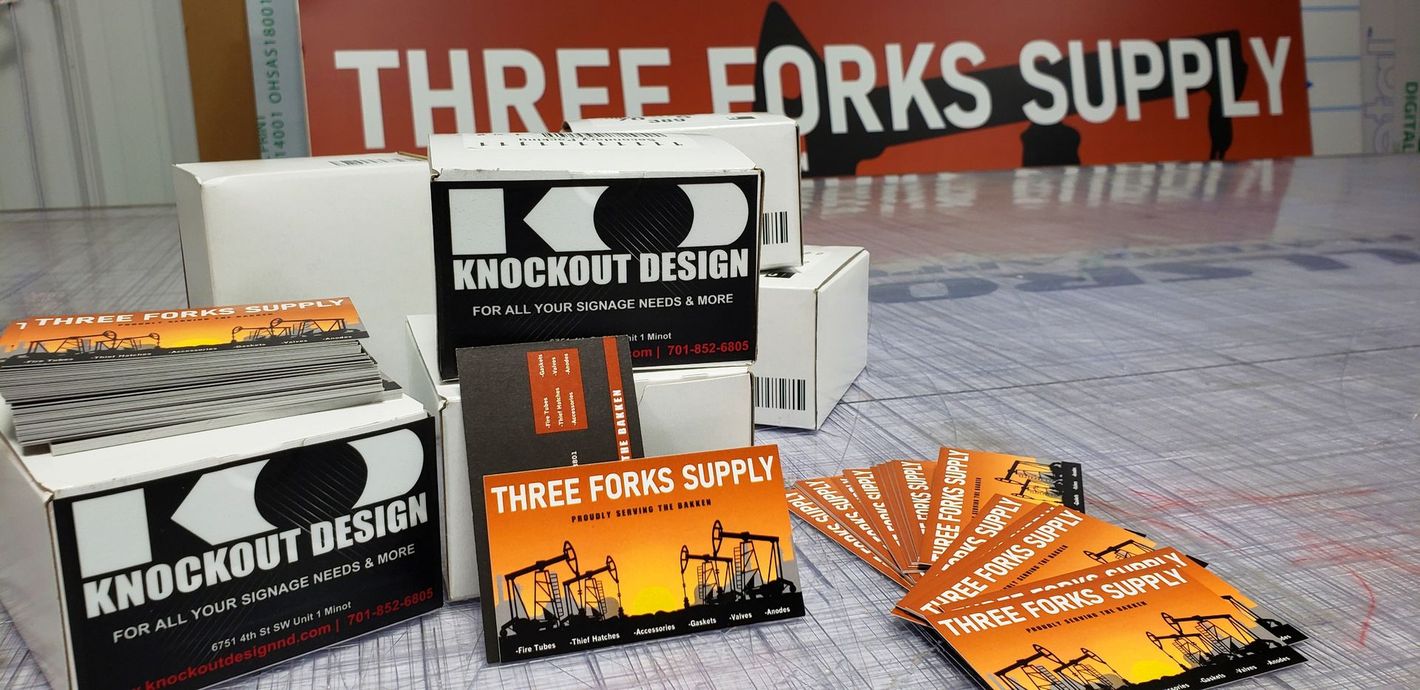 Trade show display with THREE FORKS SUPPLY signs and Knockout Design promotional materials on a table
