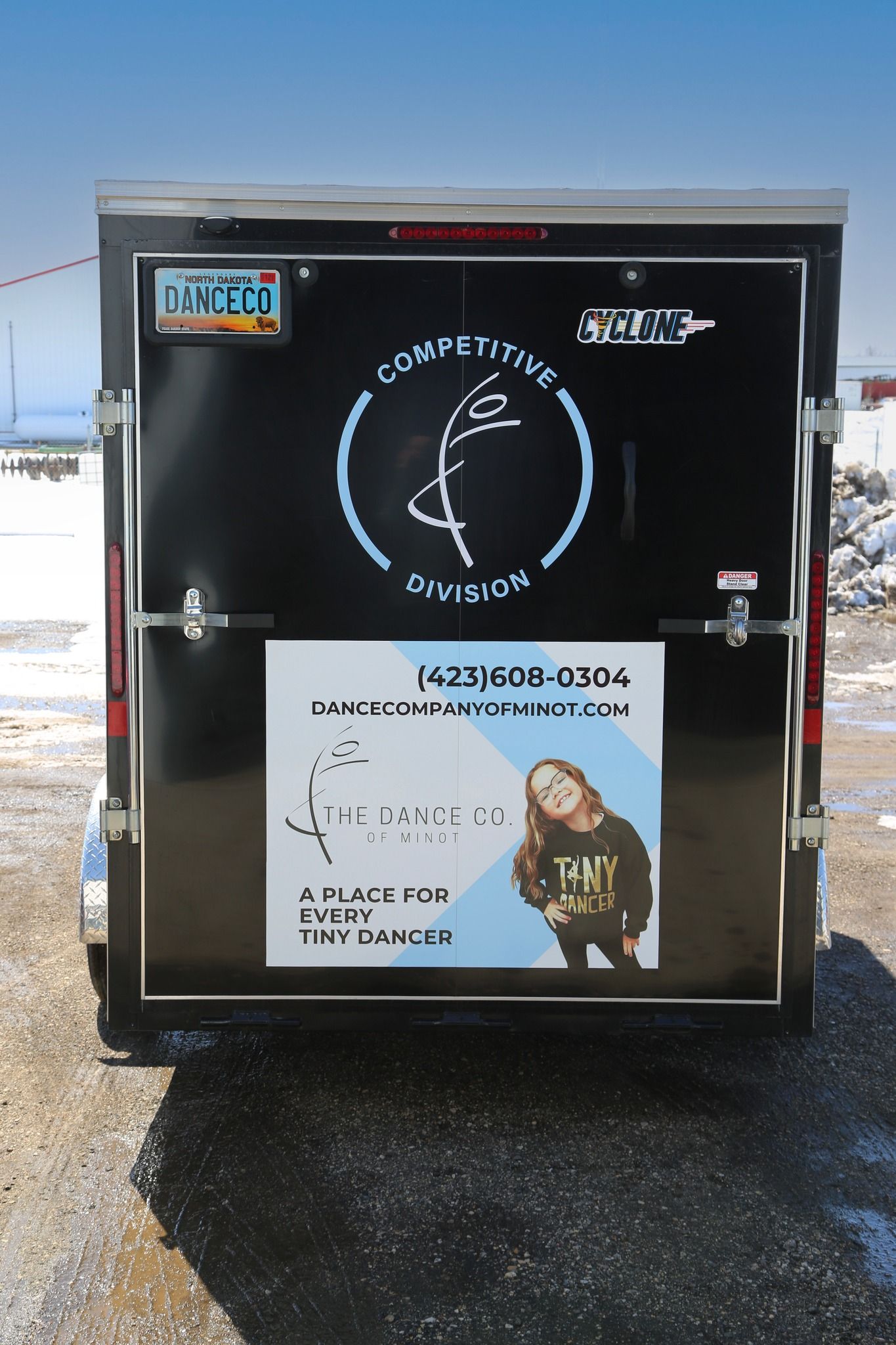 Black trailer door with decals and a poster, parked on a snowy roadside.