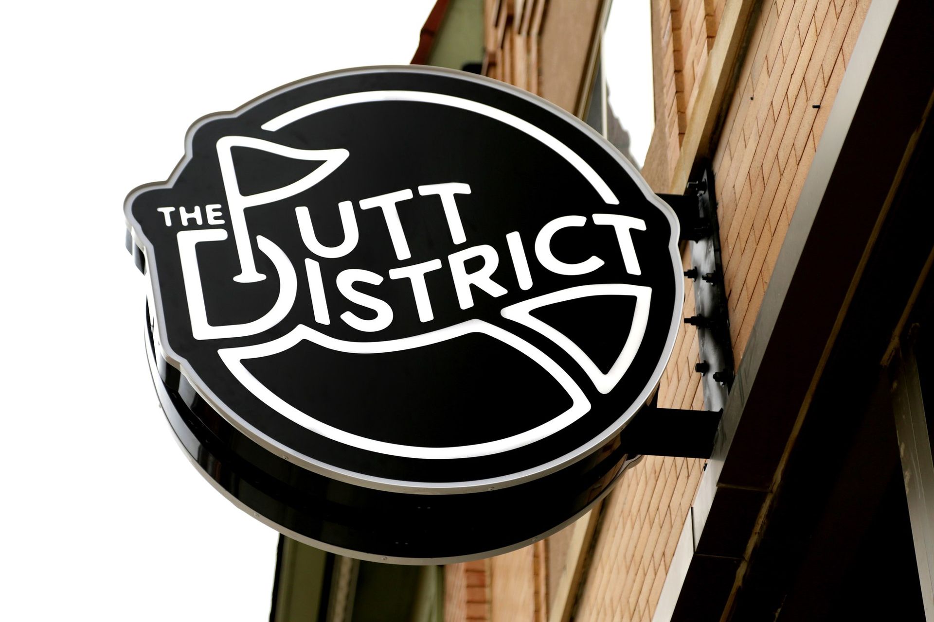 Round black sign reading “The Putt District” on a building exterior.