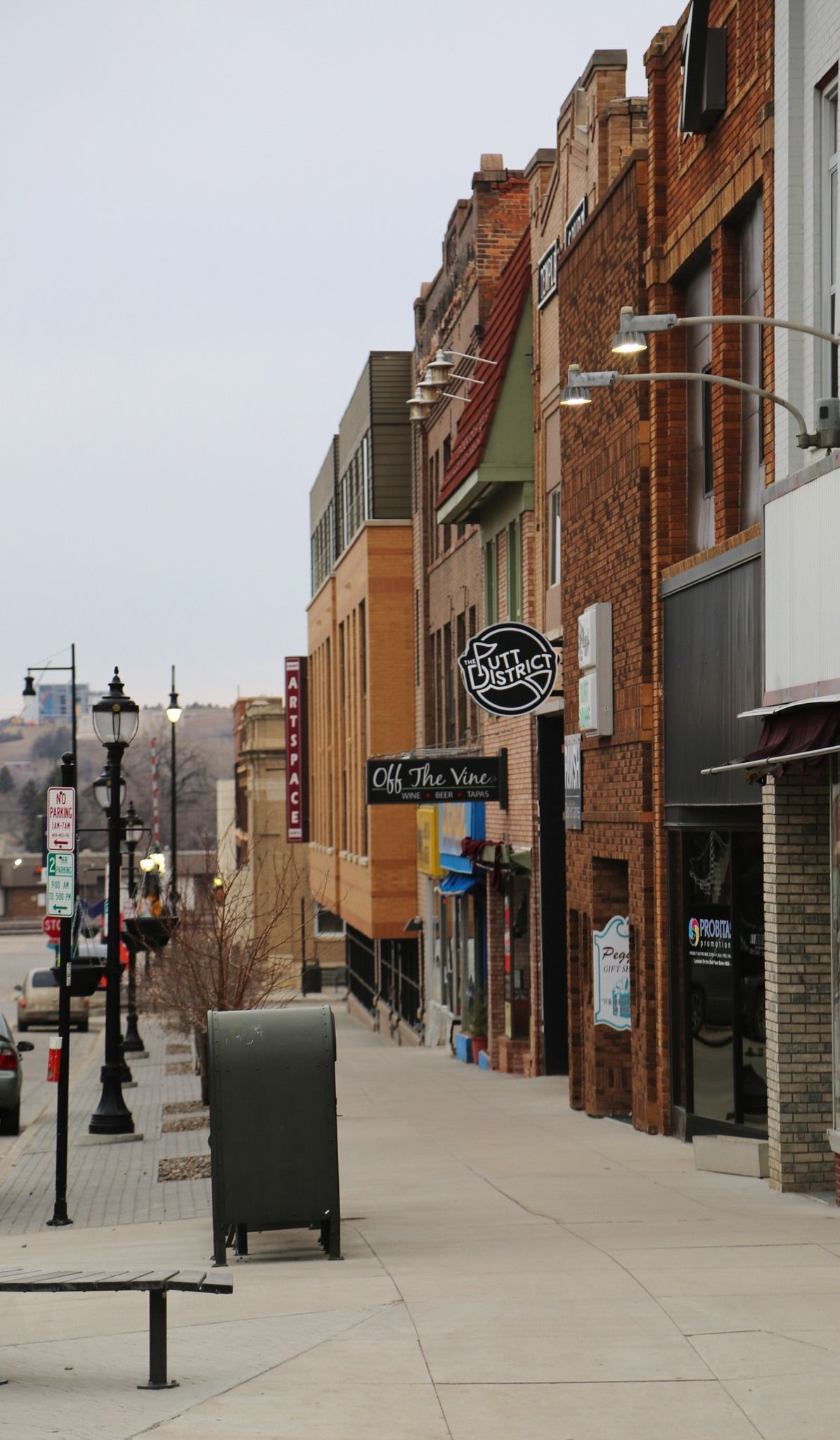 Quiet downtown sidewalk lined with brick storefronts and street signs on an overcast day