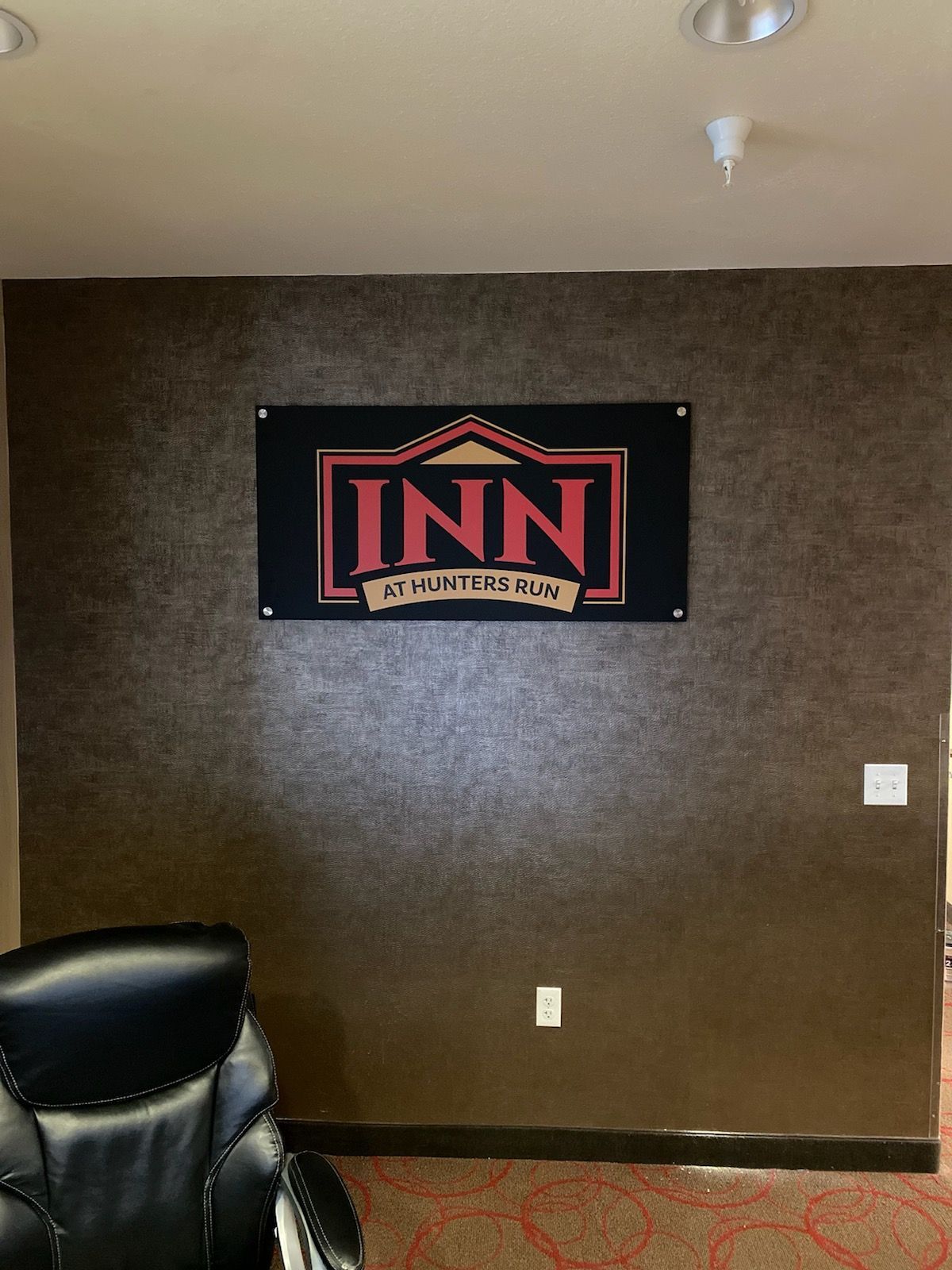 Wall with an “INN” sign and a black leather chair in a plain lobby room.