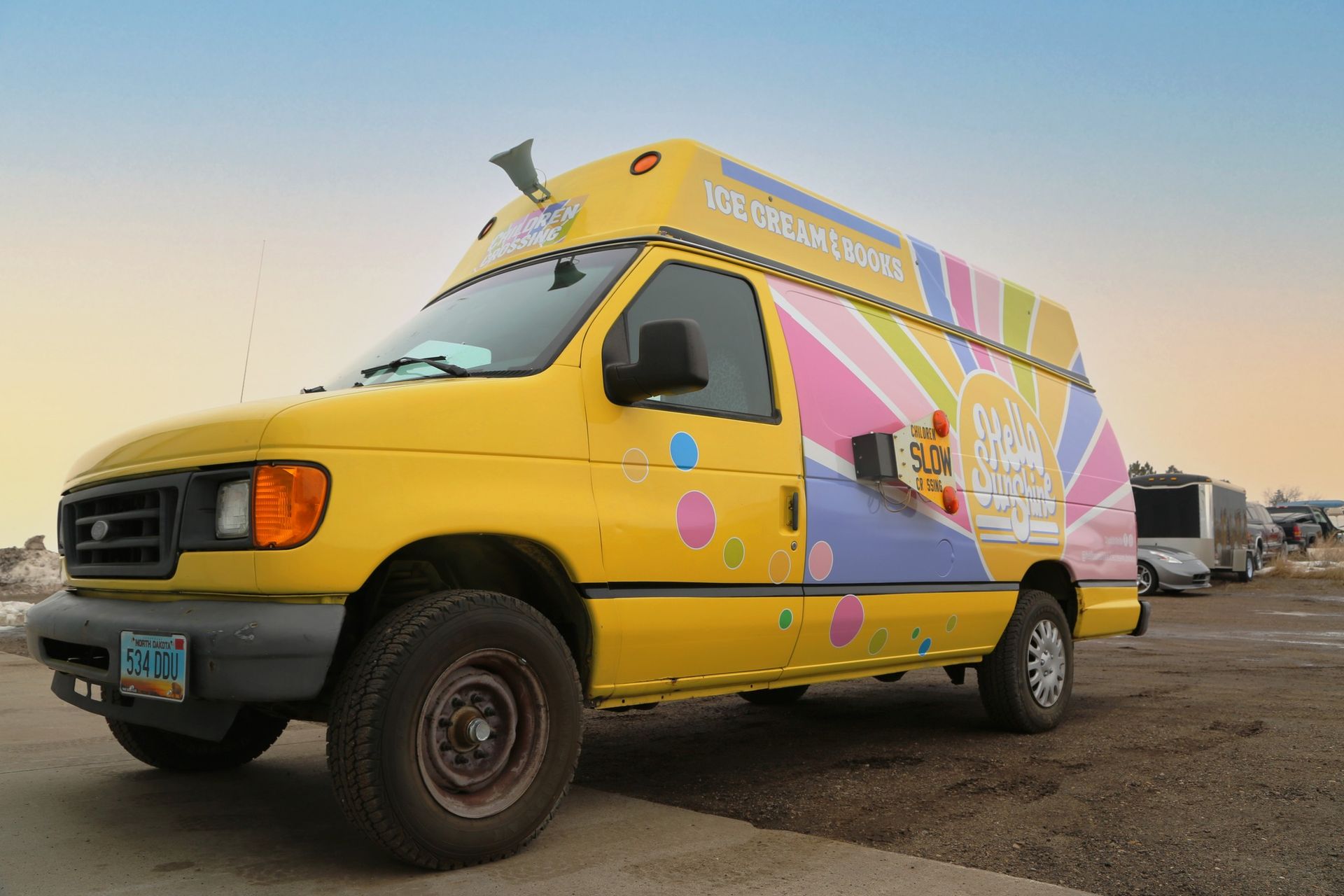 Yellow and pink branded van parked on a dirt lot at sunset