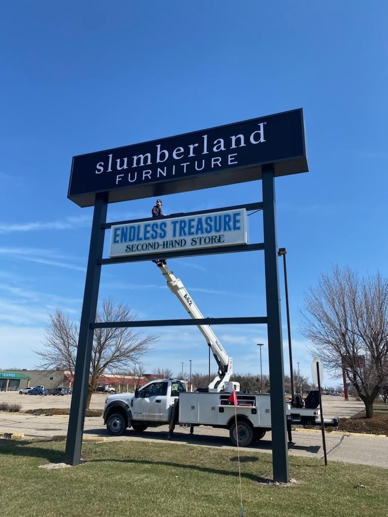 Slumberland Furniture and Endless Treasure signs by a white truck with a raised crane arm.