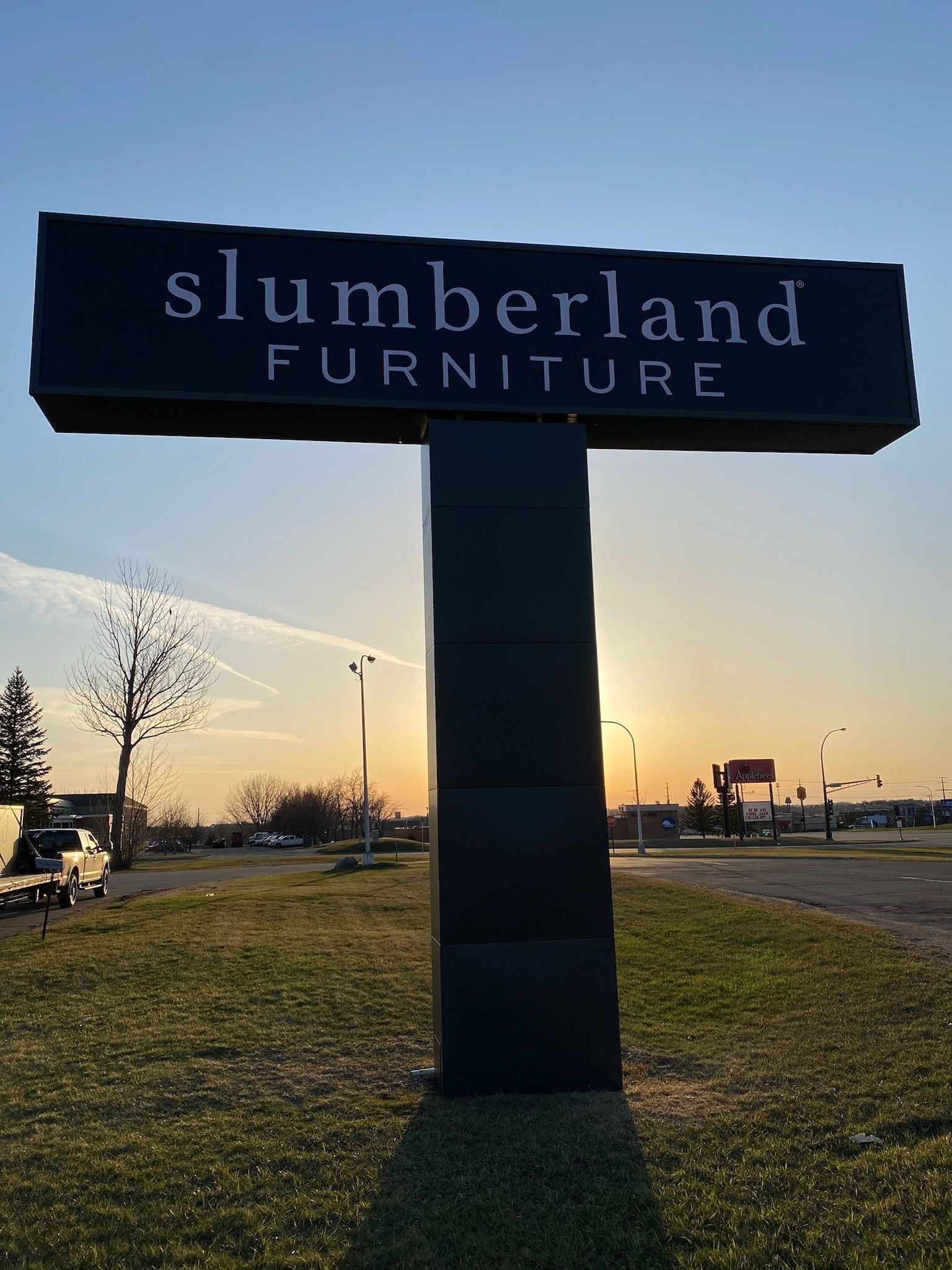 Slumberland Furniture roadside sign at sunset with a grassy lot and distant buildings