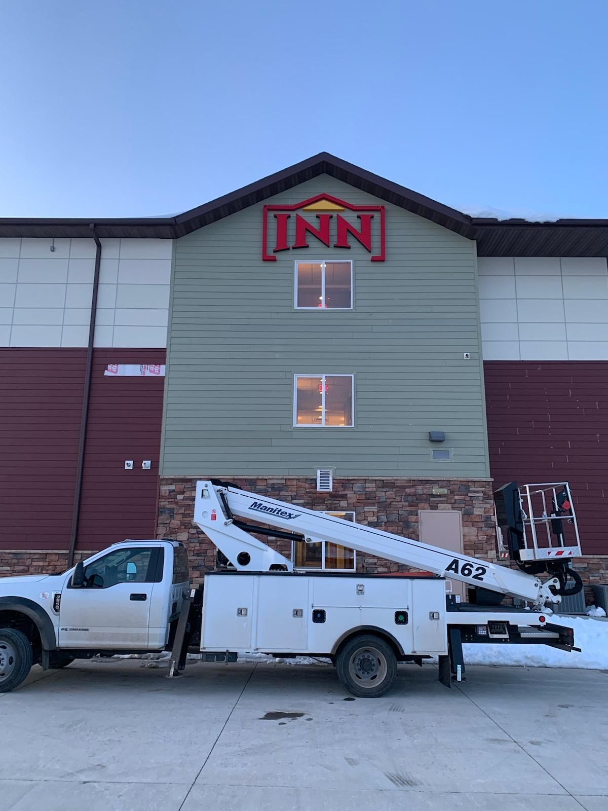 White utility truck parked in front of an INN building with a lift boom raised against the facade