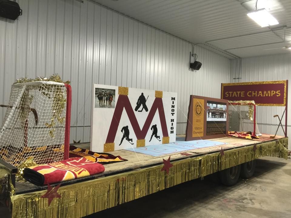 Decorated school float with maroon-and-gold pennants, large “M,” and “STATE CHAMPS” sign in a warehouse
