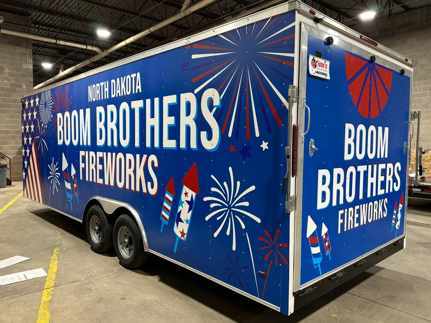 Blue Boom Brothers Fireworks trailer with red, white, and blue fireworks graphics in a warehouse.