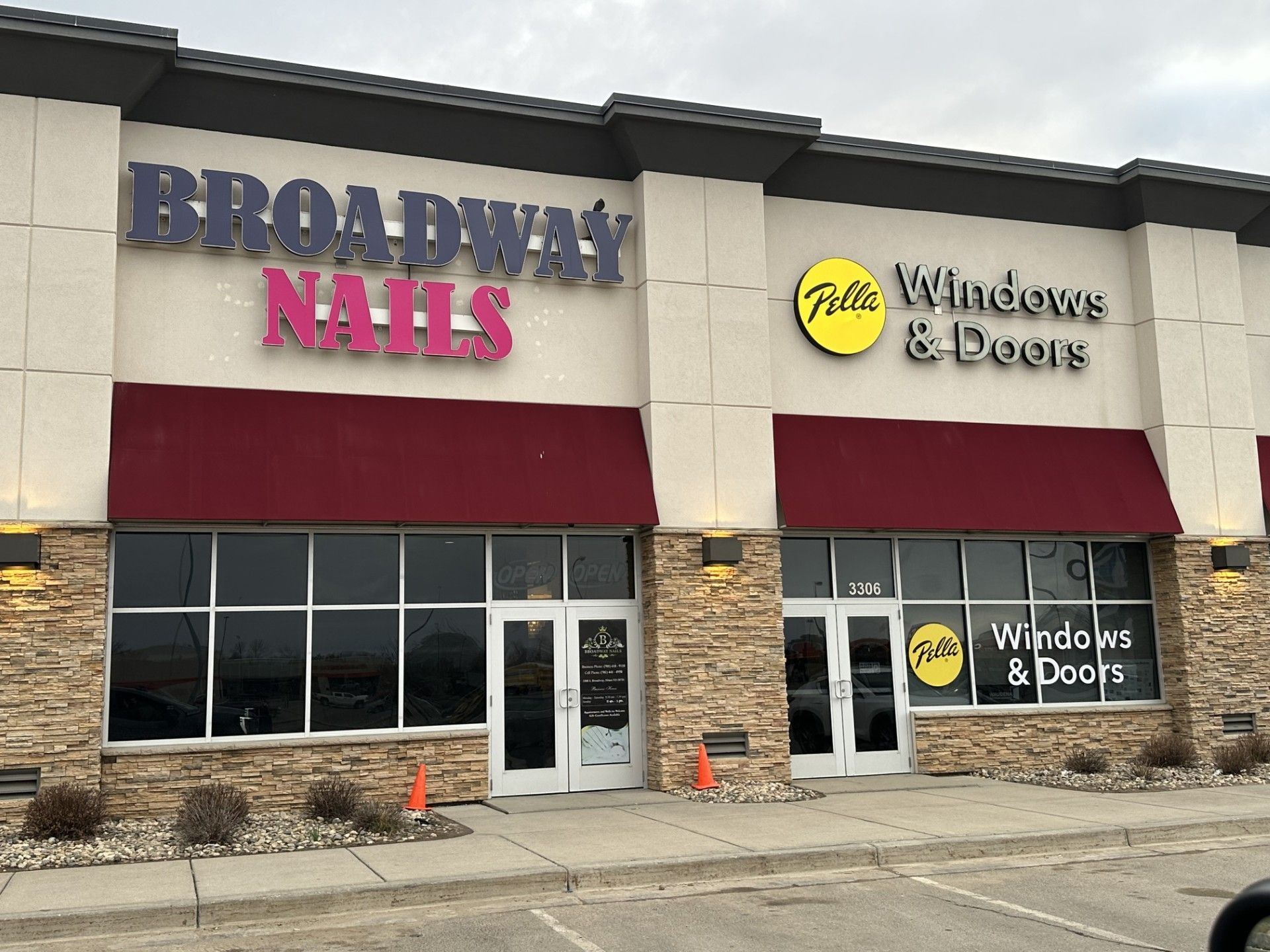 Storefronts for Broadway Nails and Pro Windows & Doors in a strip mall with red awnings