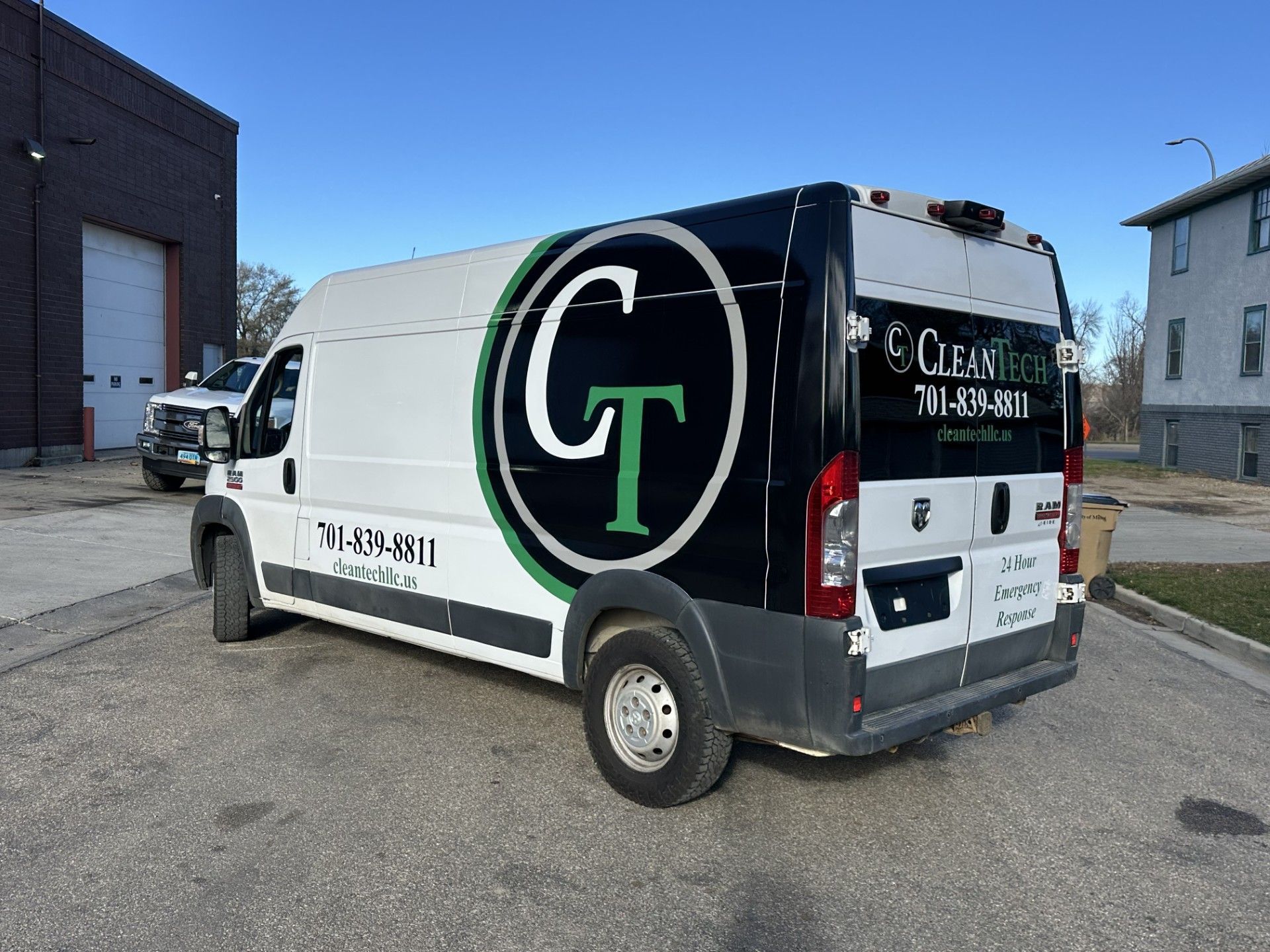 White-and-black utility van with large “CT” logo parked outside a building on a gravel lot.