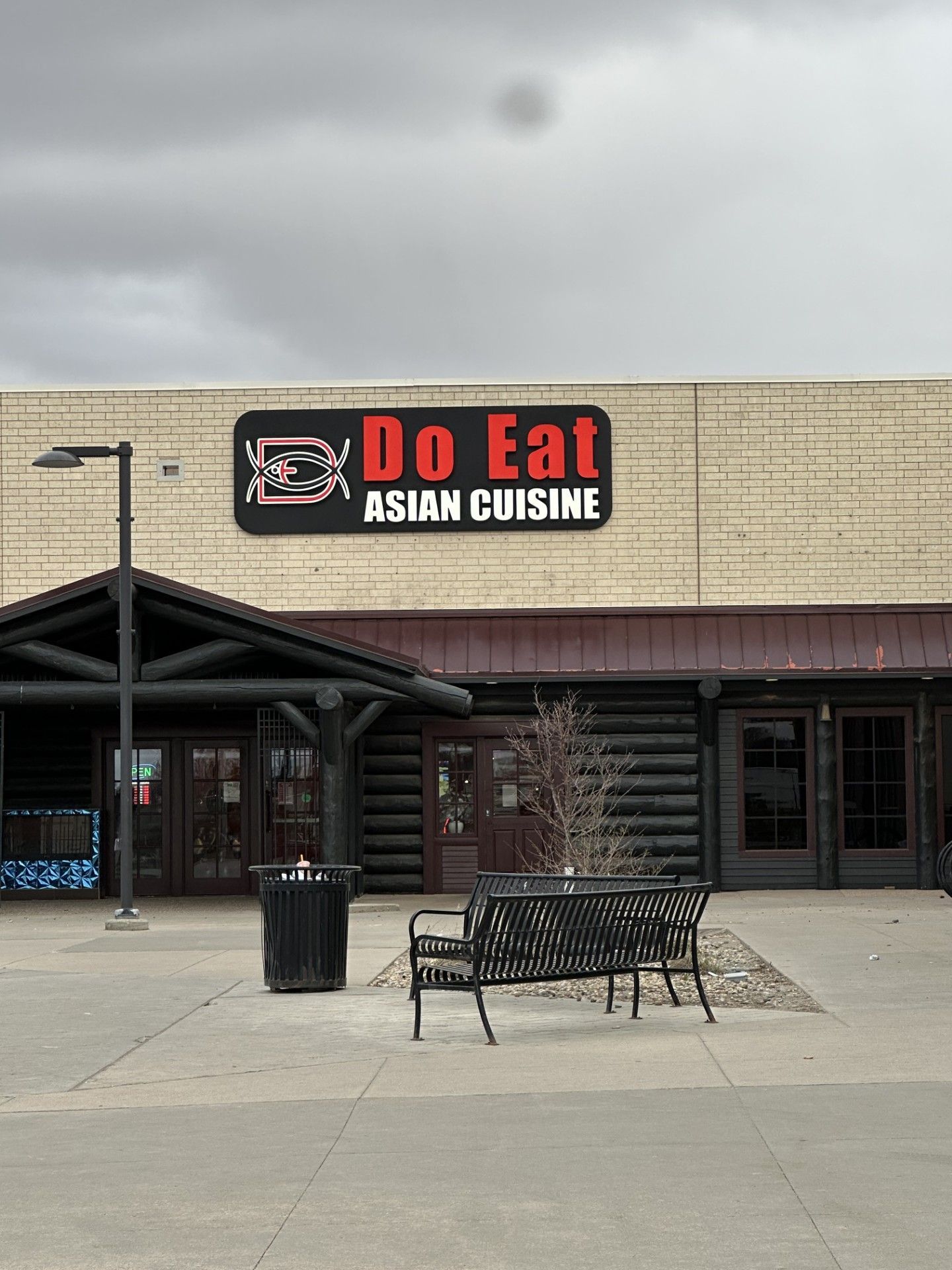 Storefront for “Oo Eat Asian Cuisine” in a strip mall with benches and a cloudy sky
