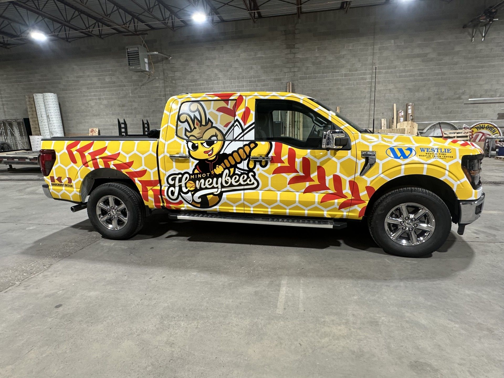 Yellow wrap truck with a cartoon bee logo parked in a warehouse garage